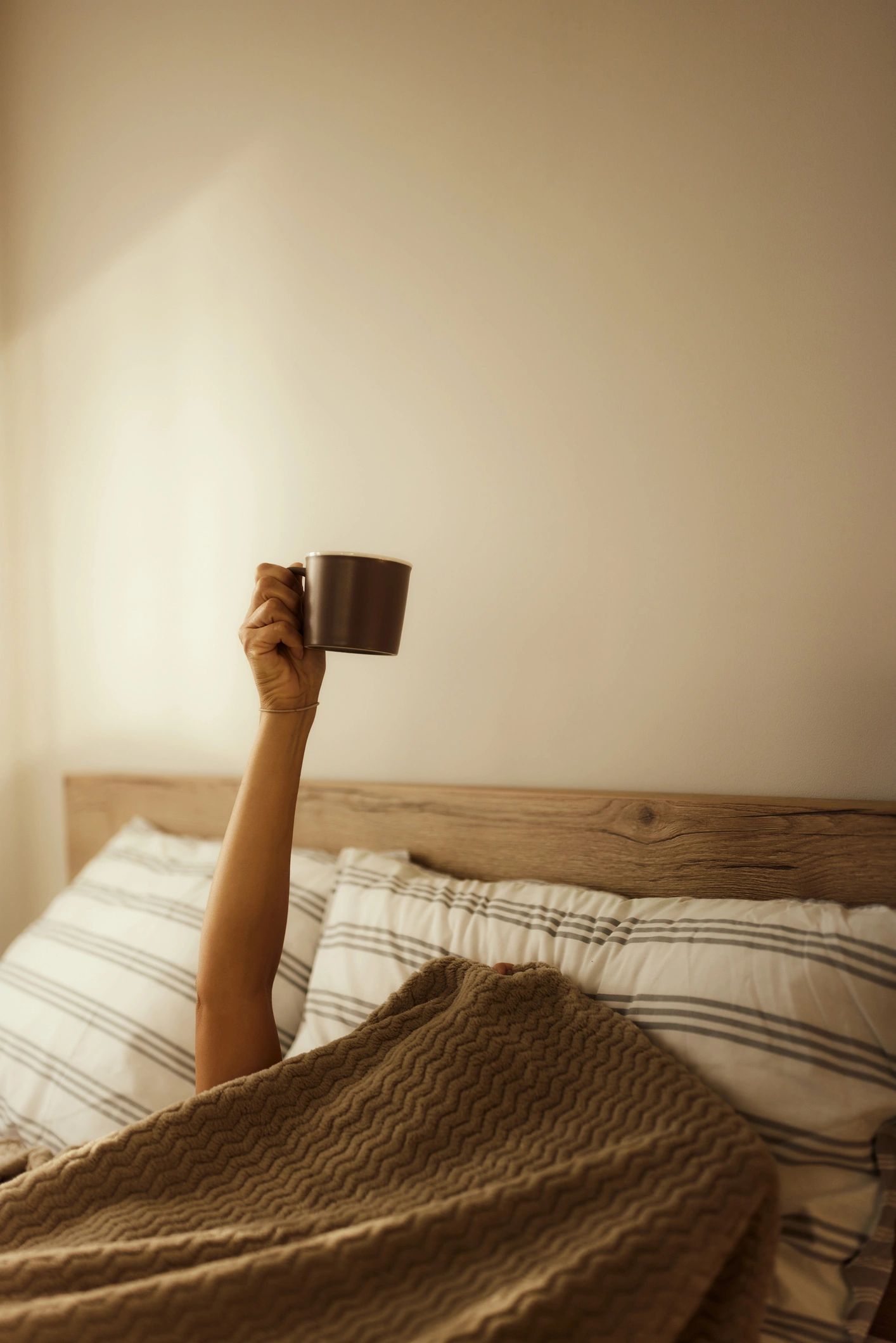 Person in bed raising a hand asking for coffee